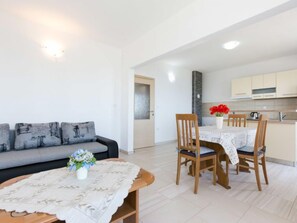 Uma sala de estar moderna com sofá, uma mesa de jantar com cadeiras e uma área de cozinha ao fundo.
