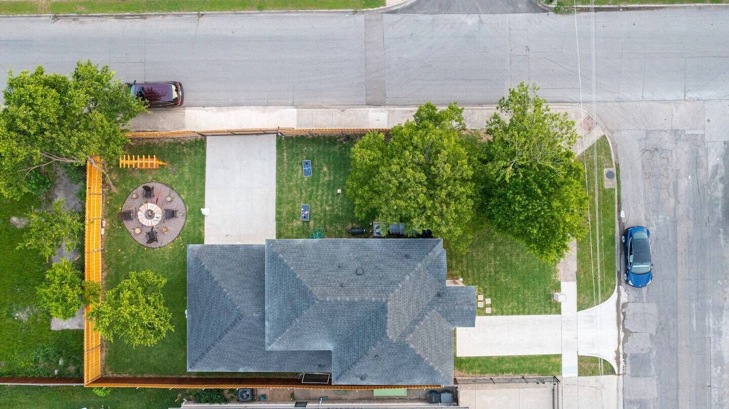 An aerial view of a building with a distinct L-shaped roof, surrounded by green lawns and trees.
