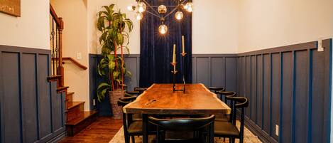 A dining room with a wooden table, black chairs, a chandelier, and a potted plant.