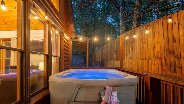 A hot tub with a wooden deck and a bench, surrounded by wooden walls and string lights. - Close 2 Parkway|Family & Dog Retreat|Game Room (Sevierville)