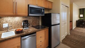 A compact kitchen with wooden cabinets, a built-in microwave, a stainless steel refrigerator, a dishwasher, and a coffee maker.