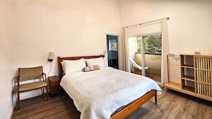 Quarto com cama de madeira, uma cadeira, mesa de cabeceira, janela com vista e prateleira de madeira.