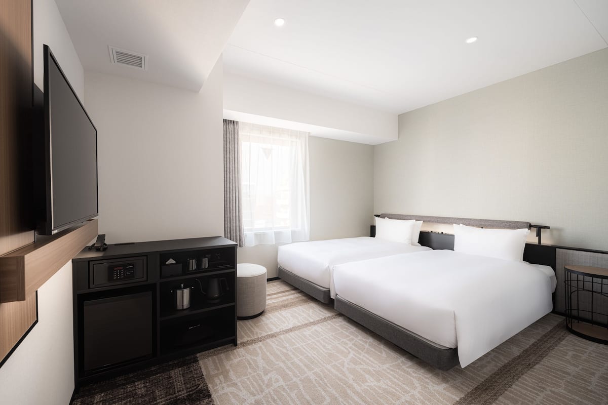 Een moderne hotelkamer met een flatscreen televisie, een minibar, een bed en een klein tafeltje.