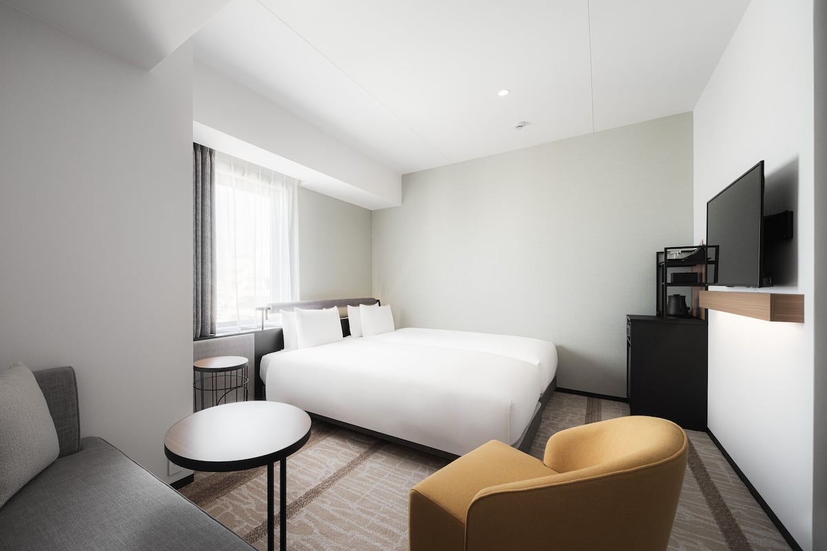 Een moderne hotelkamer met een groot bed, een bank, een klein rond tafeltje, een televisie en een bureau.