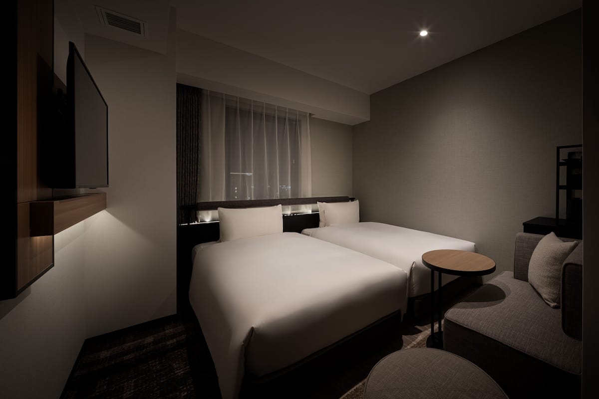 Een hotelkamer met twee bedden, een klein rond tafeltje, een bank en een televisie aan de muur.