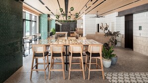 Un comedor moderno con una gran mesa de madera y sillas, rodeado de plantas en macetas y un suelo estampado.
