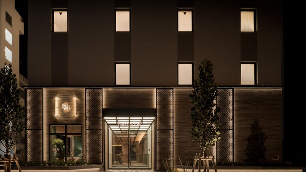 Una entrada de hotel moderna con puerta de vidrio, señalización iluminada y piso de baldosas con diseño.