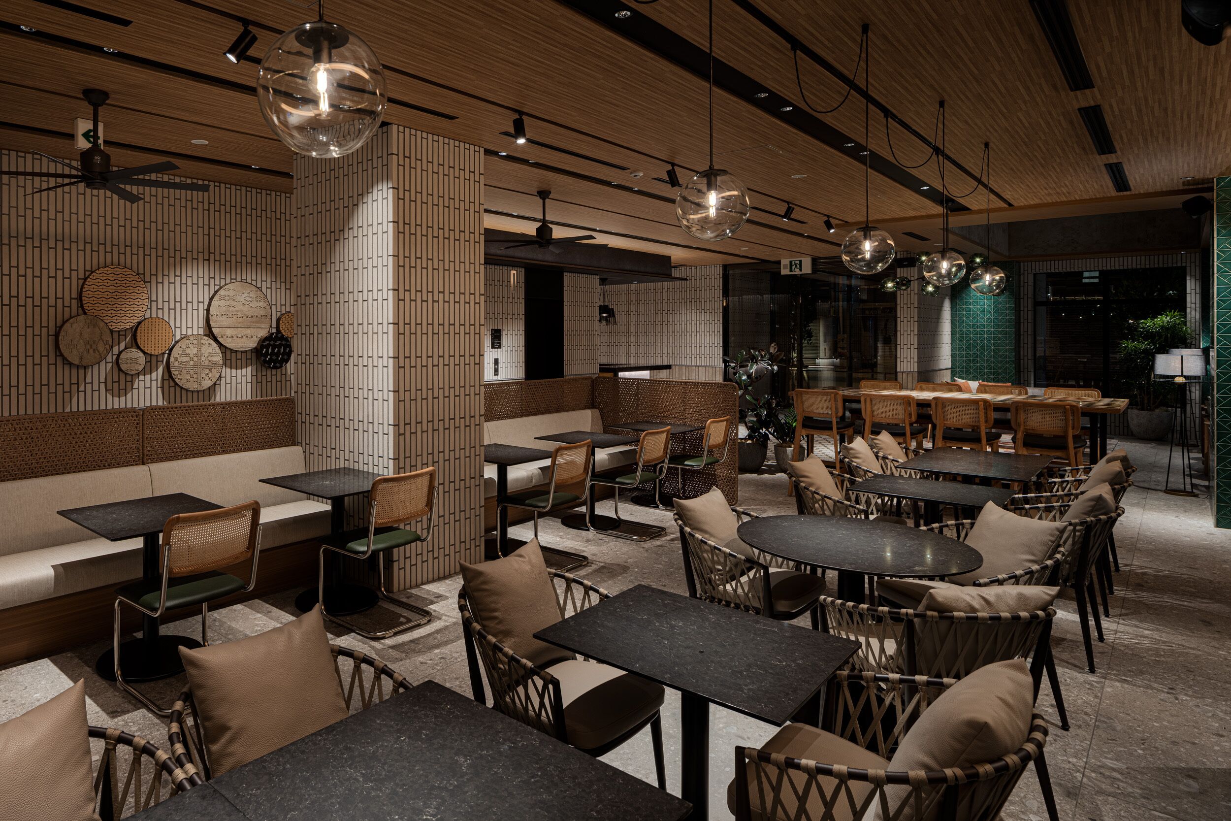A restaurant with a modern interior, featuring wooden ceiling panels, round tables, wicker chairs, and a variety of wall decorations.