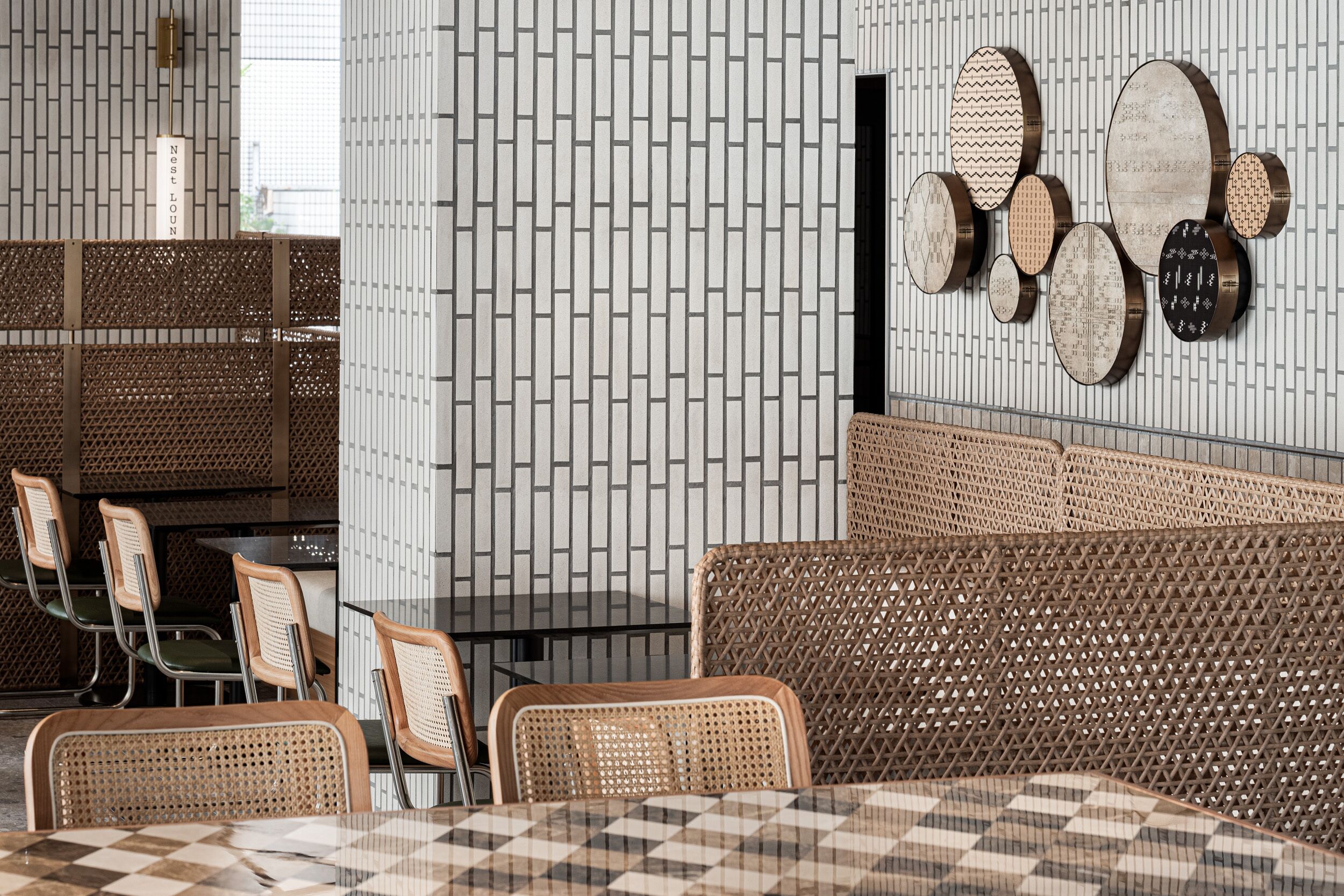 Ein moderner Essbereich mit Korbmöbeln, einem gemusterten Tisch und einer Wand mit geometrischen Mustern sowie Holzbildern.