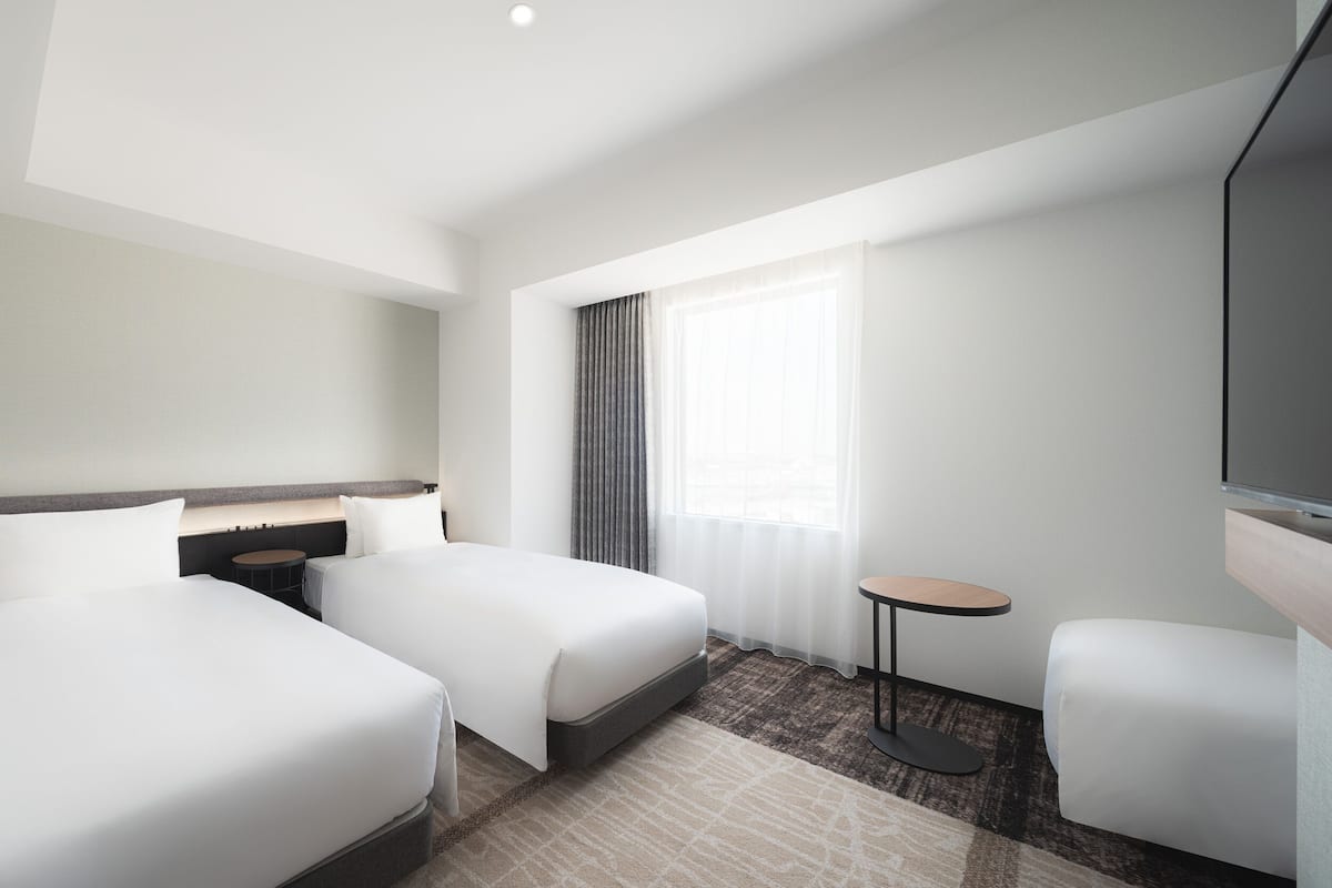 Een hotelkamer met twee bedden, een klein rond tafeltje, een televisie en een raam met gordijnen.