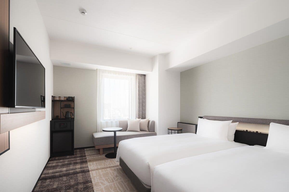Een hotelkamer met twee bedden, een bureau, een stoel, een televisie en een raam met gordijnen.