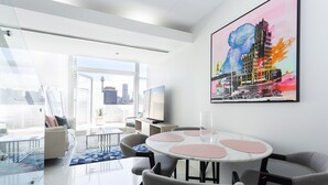 Ein moderner Arbeitsraum mit Glastrennwand, einem runden Tisch mit rosa Unterlagen und einem großen abstrakten Gemälde an der Wand.