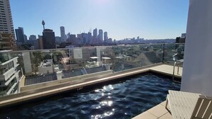 Ein Pool auf dem Dach mit Glasgeländer und Blick auf die Stadtlandschaft.