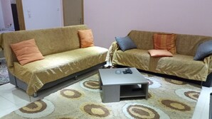 Zwei Sofas mit Kissen, ein Couchtisch und ein gemustertes Teppich im Raum, mit einer Tür und einem Lichtschalter an der Wand.