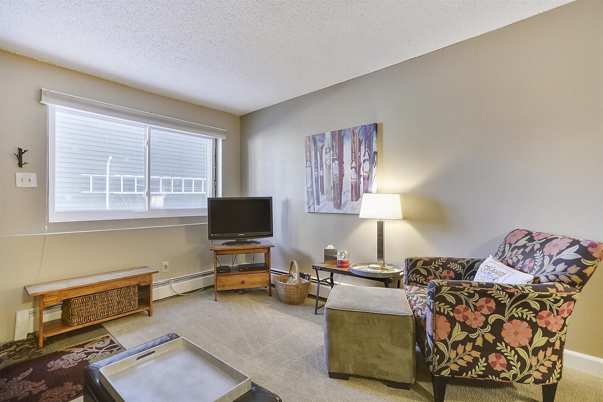 A living room with a television, a floral armchair, a side table, a lamp, and a painting on the wall.