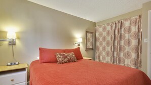 A hotel room with a bed, a nightstand, a lamp, and a curtain with a floral pattern. - Main Street Snowcave walkable to Quicksilver (Breckenridge)