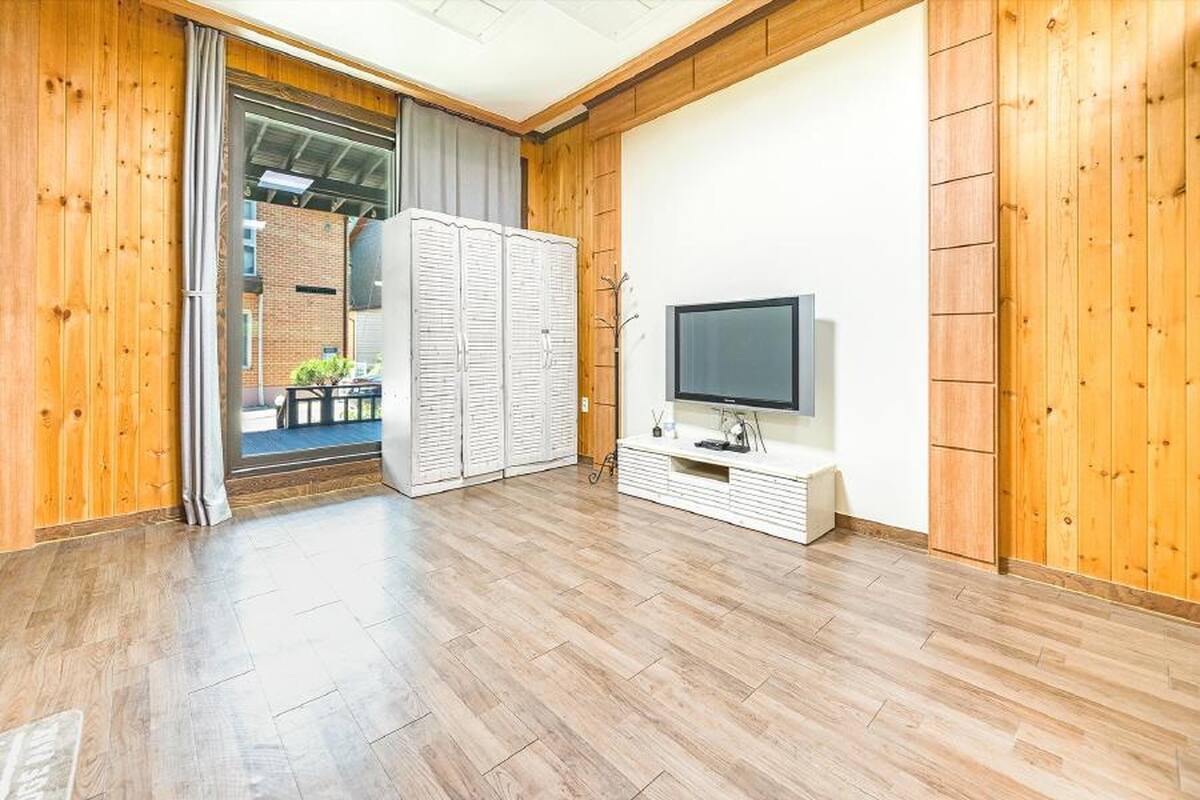 Ein Zimmer mit Holzwänden und Holzboden, einem Fernseher auf einem weißen Schrank und einer Schiebetür zu einem Außenbereich.