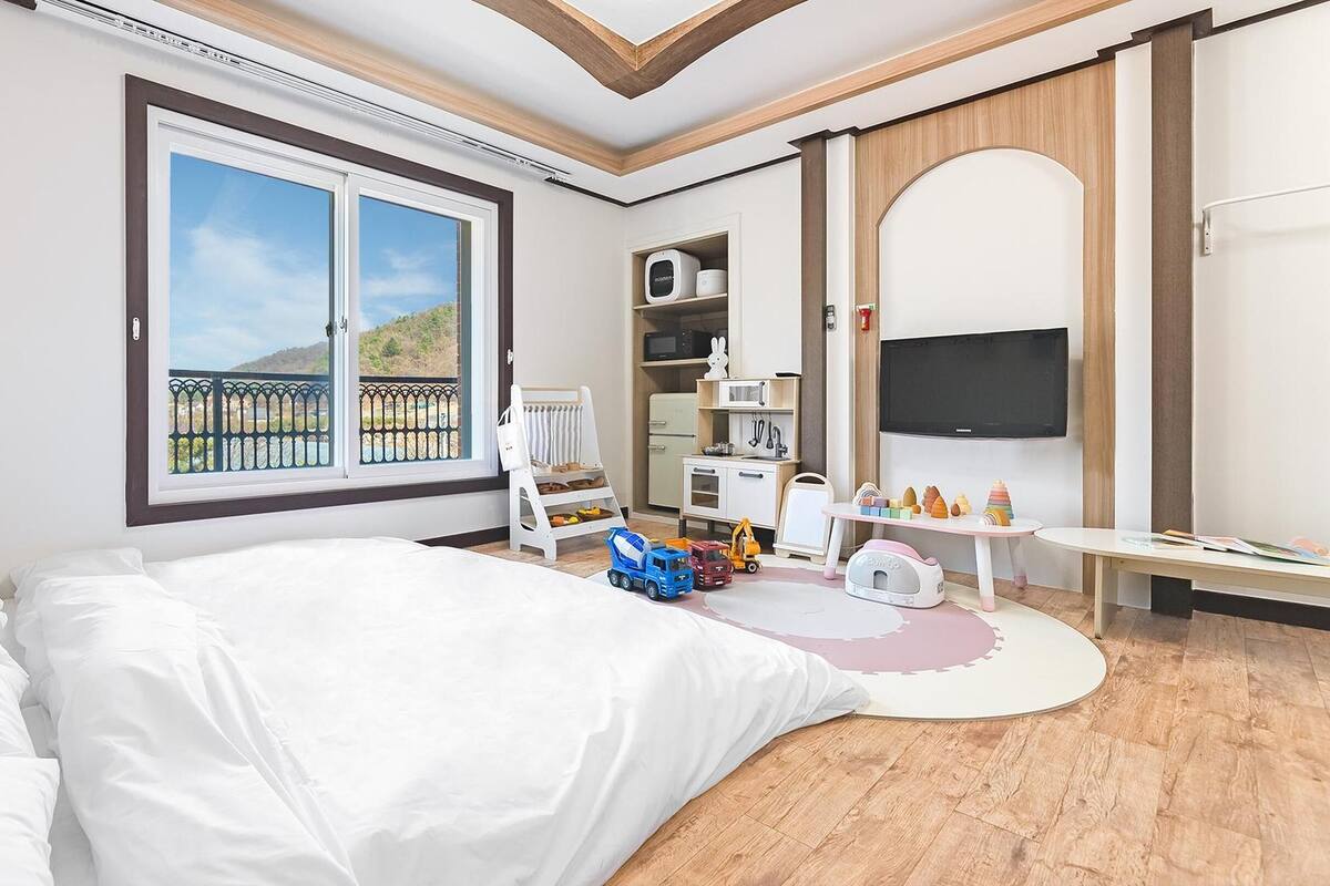 Ein Hotelzimmer mit einem großen Bett, einem Schreibtisch mit Spielzeug, einem Fernseher und einem Balkon mit Blick.