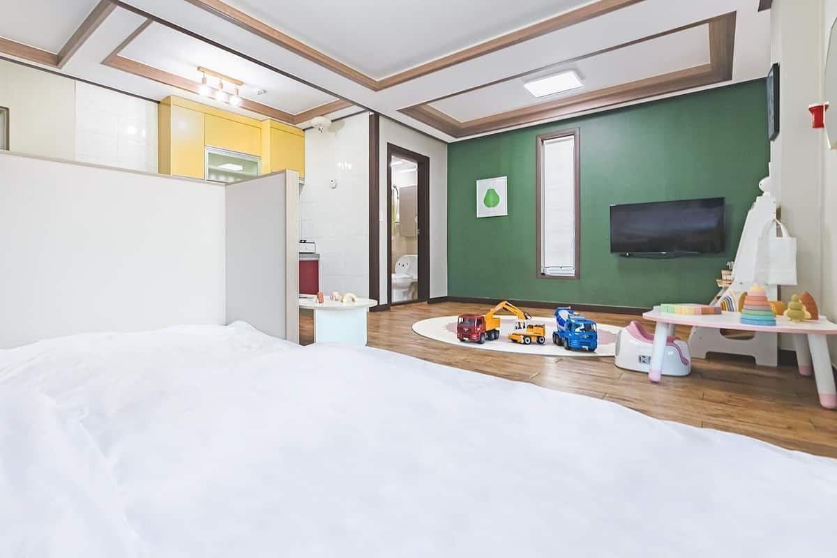 Ein Hotelzimmer mit einem Bett, einem Fernseher, einer grünen Wand und Kinderspielzeug.