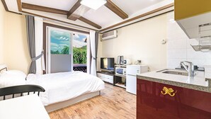 Een slaapkamer met een bed, televisie, magnetron en kitchenette met een spoelbak en kastjes.