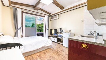 A bedroom with a bed, a TV, a microwave, and a kitchenette with a sink and cabinets.