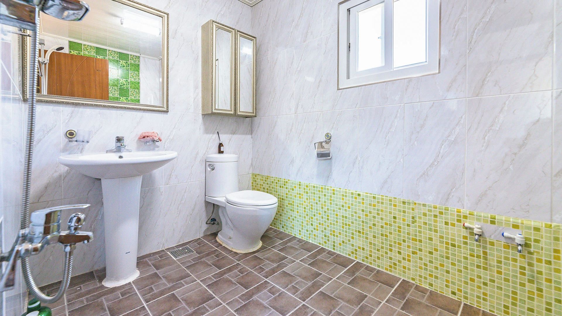 A bathroom with a white sink, a toilet, and a shower. There are two mirrors above the sink and a window above the toilet.