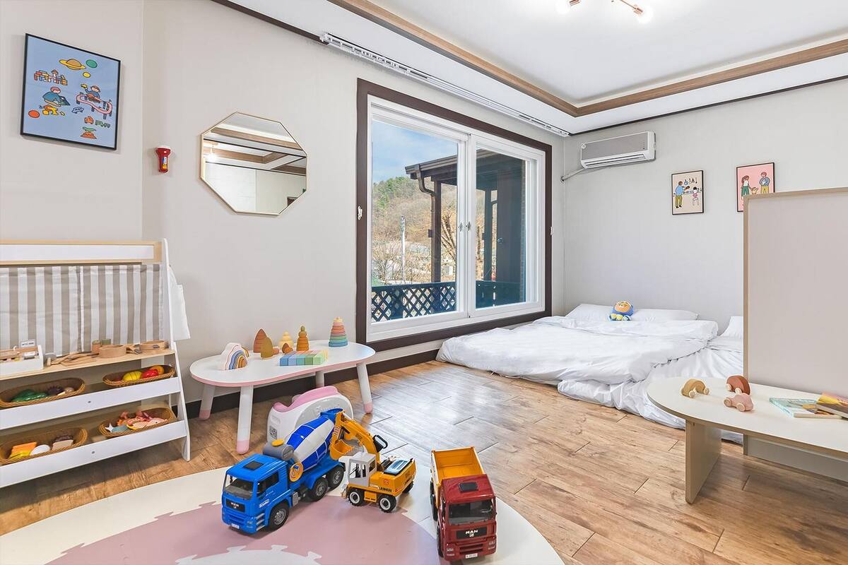 Ein Kinderzimmer mit Spielzeug, einem Bett und einem großen Fenster.