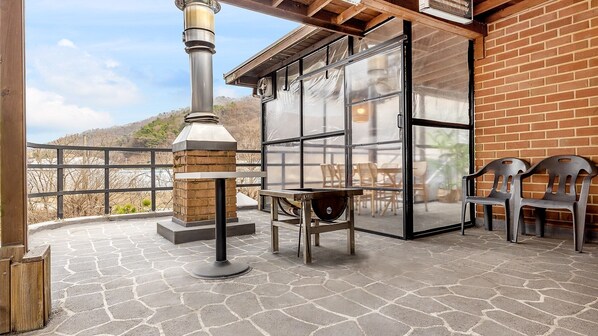 Un patio exterior con pared de ladrillo, puerta de vidrio, mesa de metal y dos sillas de plástico.
