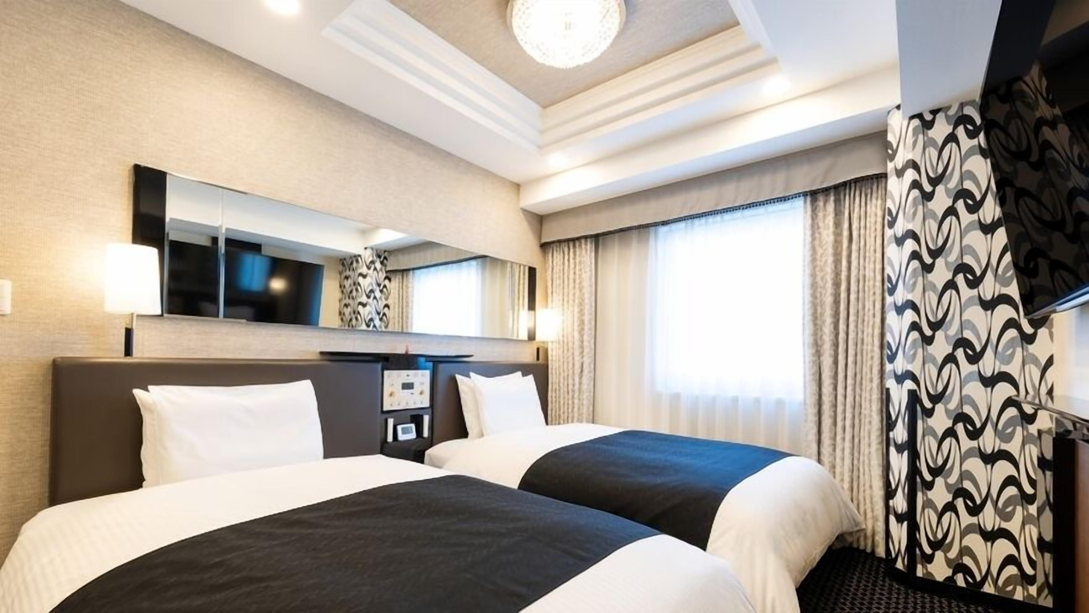A hotel room with two beds, a large mirror, a flat-screen TV, and a window with curtains.