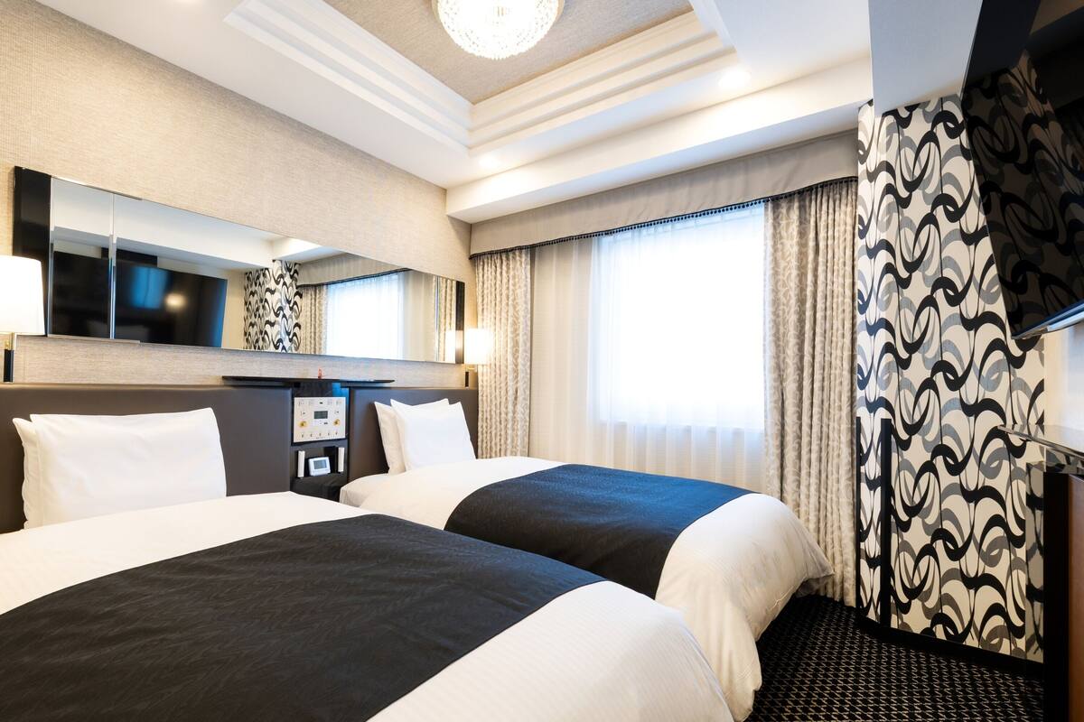 A hotel room with two beds, a large mirror, a flat-screen TV, and a patterned curtain.