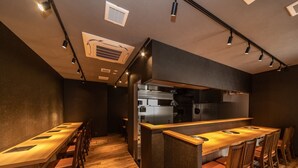 Een modern restaurantinterieur met een lange houten bar, meerdere zithoeken en een keuken door een scheidingswand zichtbaar.