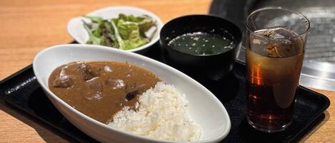 Un plato que incluye arroz, curry, una ensalada y una bebida, sobre una bandeja.