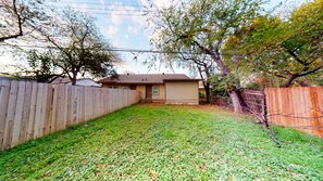 Enjoy the serene atmosphere of this backyard with a grassy lawn and a charming single-story home.