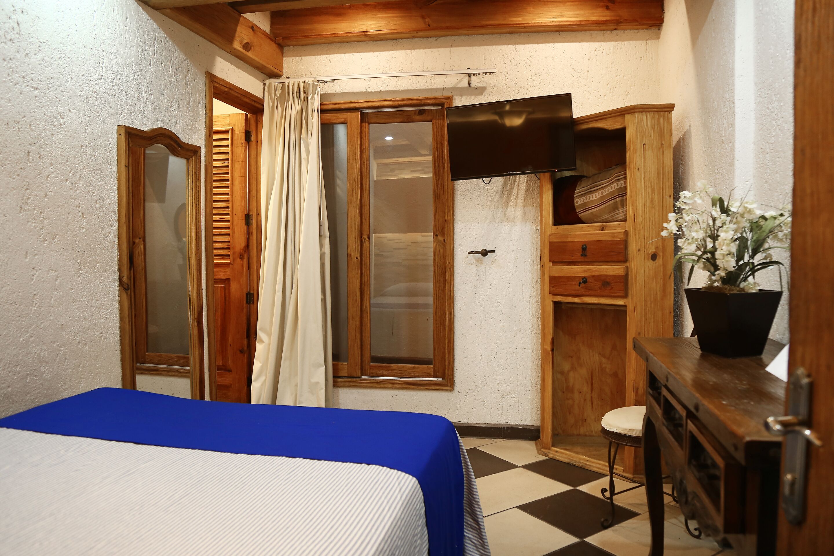 Un dormitorio con cama, armario de madera, taburete pequeño y planta en maceta.