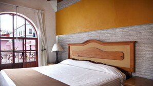 A bedroom with a large bed, a wooden headboard, a nightstand with a lamp, and a view through a window with curtains.