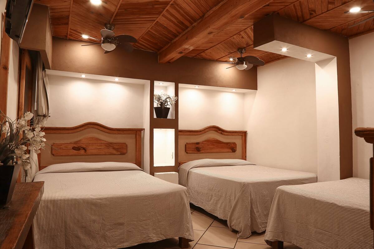 A room with two beds, wooden headboards, ceiling fans, recessed lighting, and a potted plant.