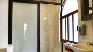 A bathroom with a glass shower door, a toilet, a sink, and a window.
