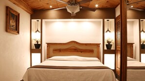 A bedroom with a wooden headboard, two bedside tables with potted plants, and a ceiling fan.