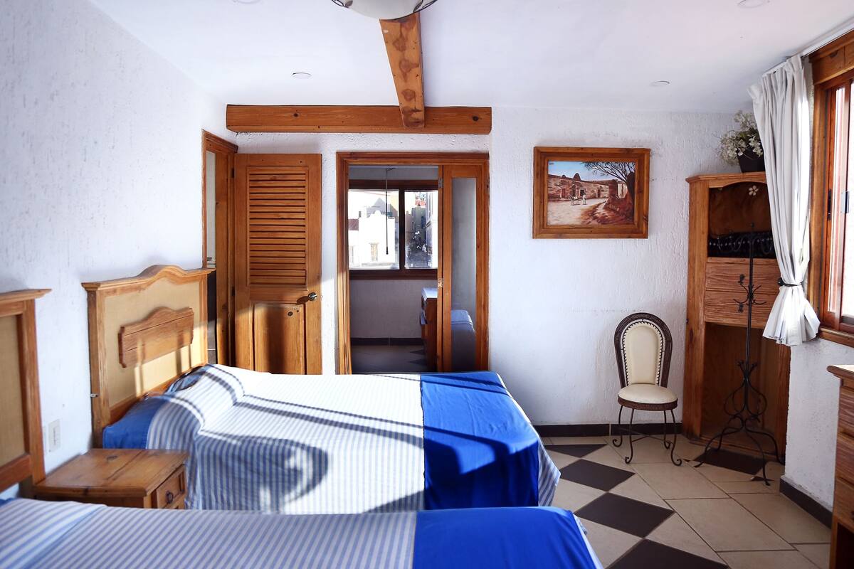 A bedroom with two beds, wooden furniture, a chair, and a painting on the wall.