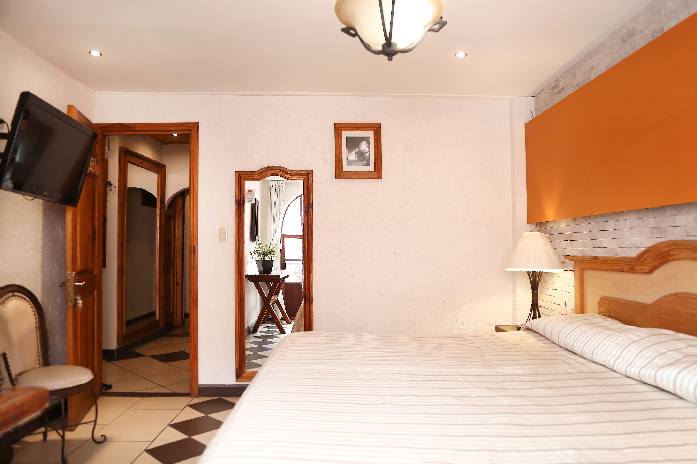 Una habitación de hotel con cama, televisor, escritorio con silla, espejo y lámpara.
