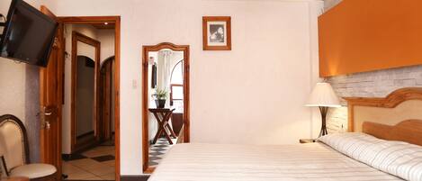 Una habitación de hotel con cama, televisor, escritorio con silla, espejo y lámpara.