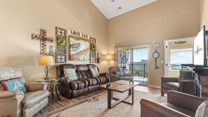 A spacious living room with leather sofas, a coffee table, and a large window offering a view of the outdoors. - Table Rock View Penthouse with Sun Room, Luxury Decor, Free Tickets & Prime Location (Branson)