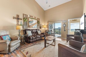 A spacious living room with leather sofas, a coffee table, and a large window offering a view of the outdoors. - Table Rock View Penthouse with Sun Room, Luxury Decor, Free Tickets & Prime Location (Branson)