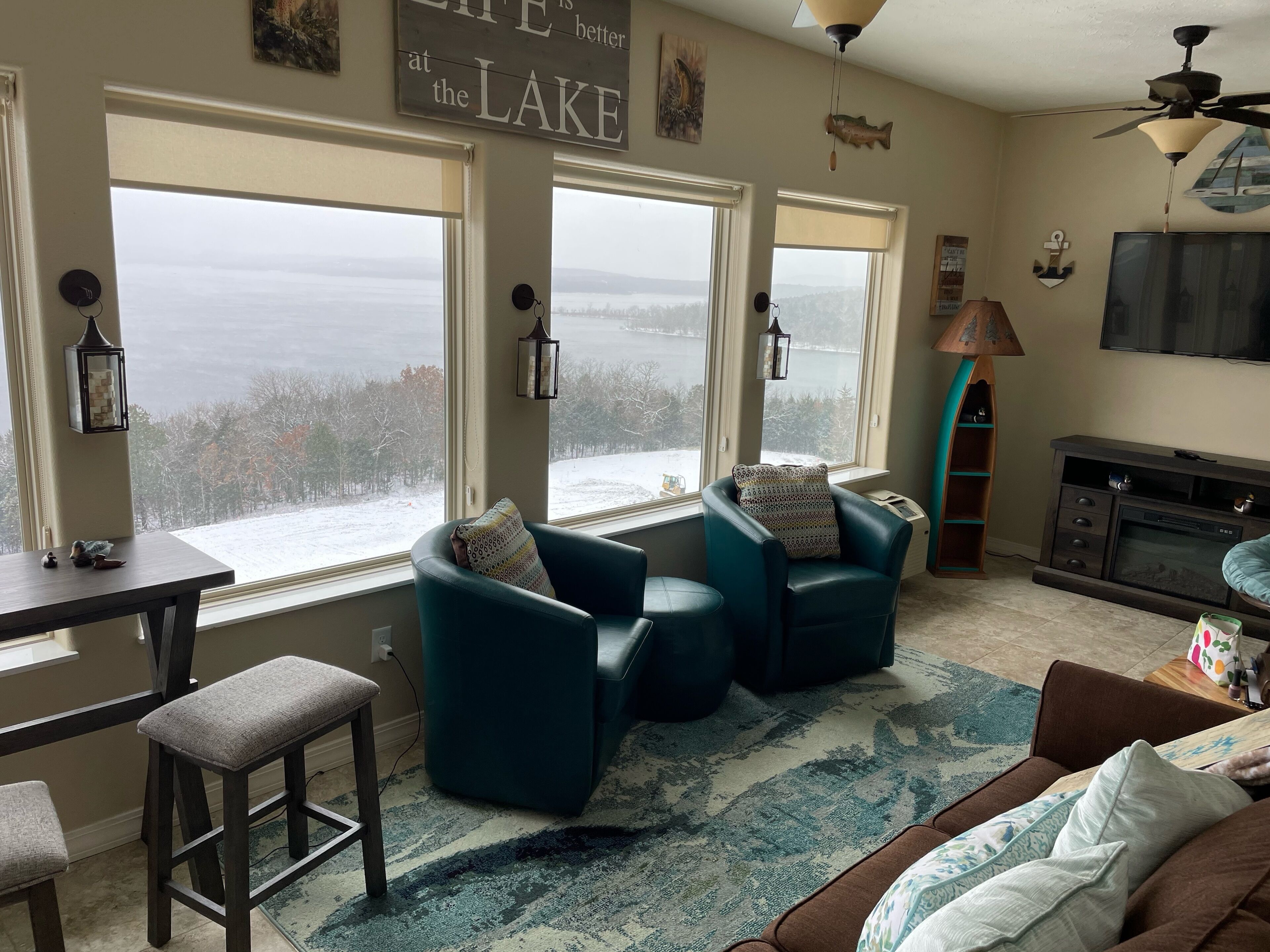 A living room with large windows, a ceiling fan, and a fireplace.