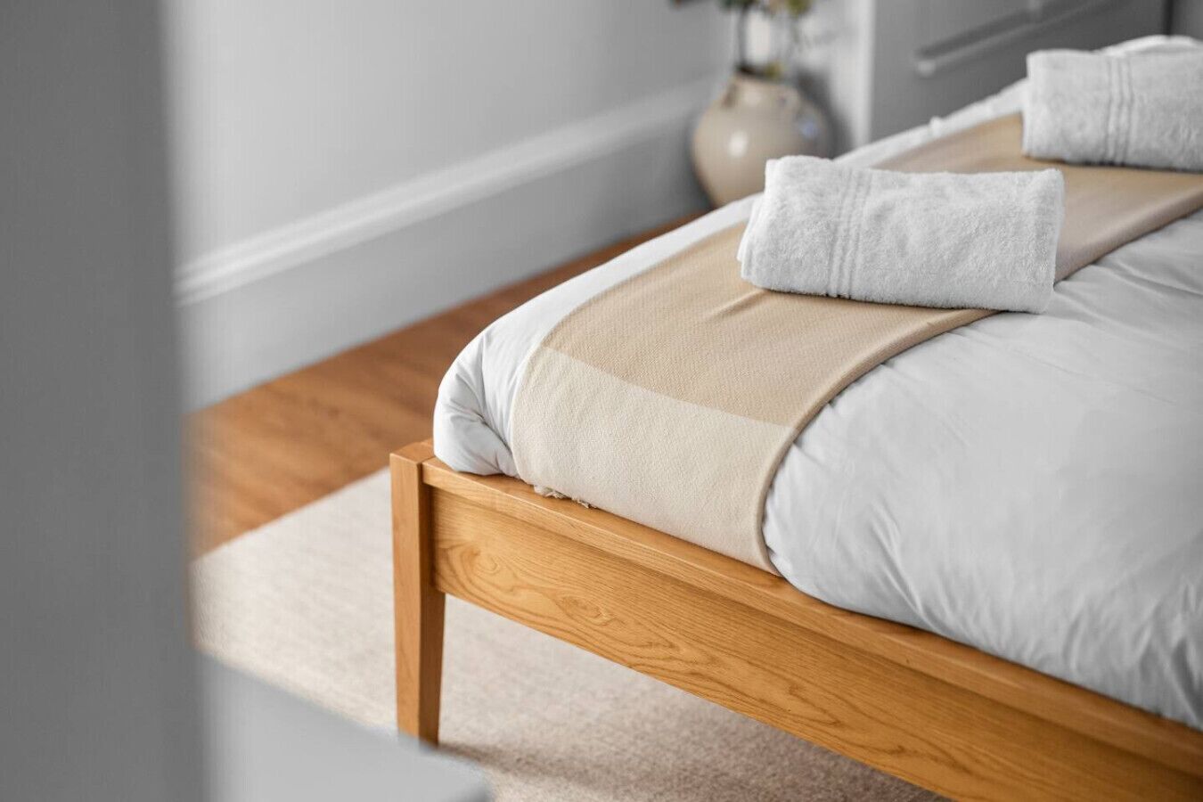 A neatly made bed with a wooden frame, white and beige bedding, and a white towel on the side.