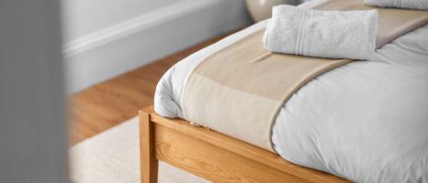 A neatly made bed with a wooden frame, white and beige bedding, and a white towel on the side.