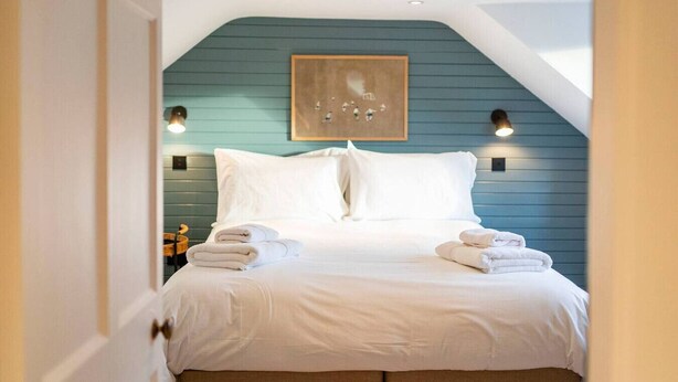 A bedroom with a bed, white bedding, a teal accent wall, and two wall-mounted lights. - Regal Residence - Metropolitan Luxury (Broughty Ferry, Dundee)