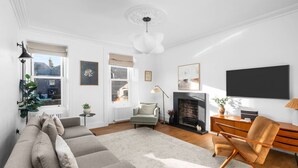 A modern living room with a sectional sofa, a fireplace, a dining area with a wooden table and chairs, and a large window providing natural light. - Regal Residence - Metropolitan Luxury (Broughty Ferry, Dundee)