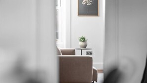 A modern living room with a beige sofa, a small round table with a plant, and a framed picture on the wall. - Regal Residence - Metropolitan Luxury (Broughty Ferry, Dundee)