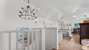 A spacious living area with a white railing, a chandelier, and a large window. - Dejarnette Cottage w/Private Courtyard & Pool | 30A Rosemary Beach | My Beach Getaways (Rosemary Beach)